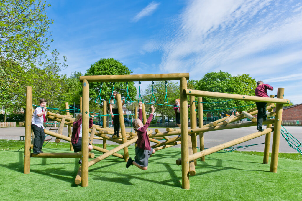 Several children in school uniforms play and climb on a large wooden playground structure outdoors on a sunny, partly cloudy day, emphasising the importance of maintaining playground equipment for safety and fun.