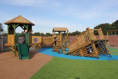Children play on a wooden playground structure with slides, climbing nets, and a lookout tower on a sunny day, making playgrounds more creative with exciting features that inspire imaginative adventures.