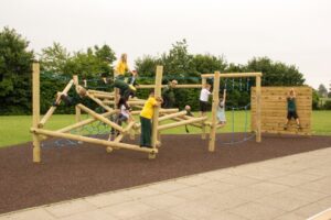 Children play and climb on a wooden playground structure with ropes and a climbing wall, set on a rubber surface in a grassy outdoor area—perfect for getting enough outdoor activity.