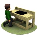A child in a green jumper kneels on grass in front of a wooden table with a black rectangular object on top.