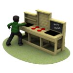 A child stands at a wooden play kitchen labelled Messy Kitchen, with red circular objects on the counter, on a patch of artificial grass.