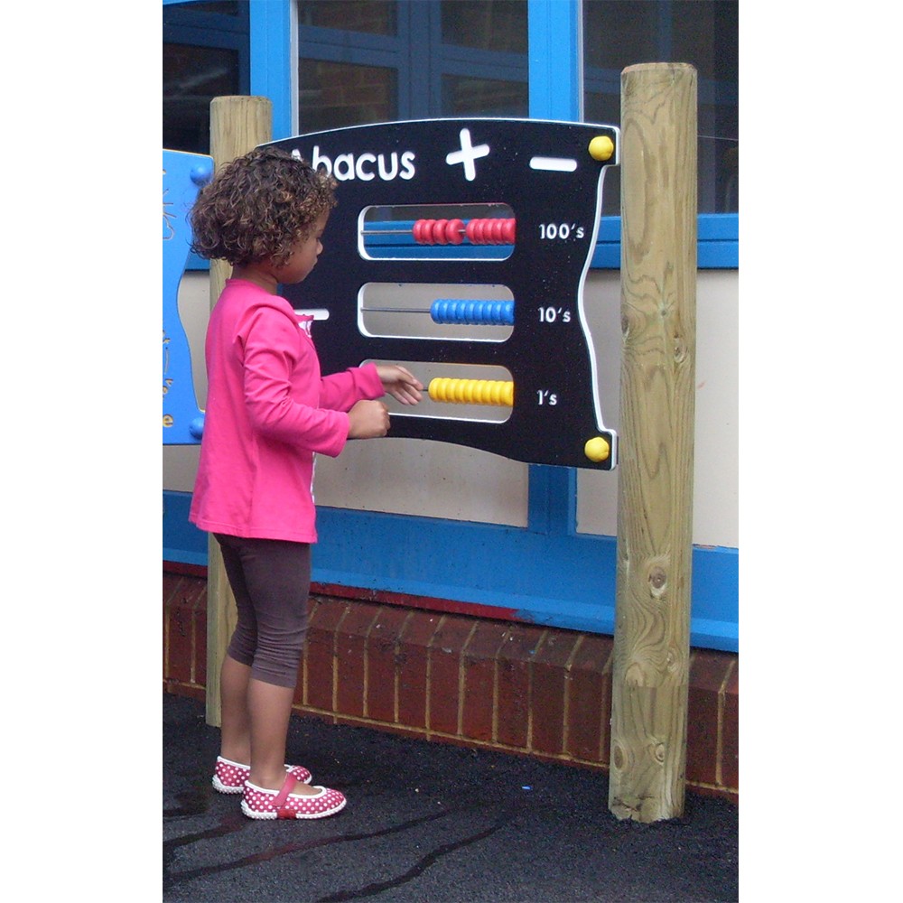 A young child stands outdoors using a large abacus with coloured beads mounted on a black board labelled for hundreds, tens, and ones.