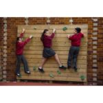 Three children in school uniforms climb a wooden Single Sided Bouldering Wall attached to a brick wall.