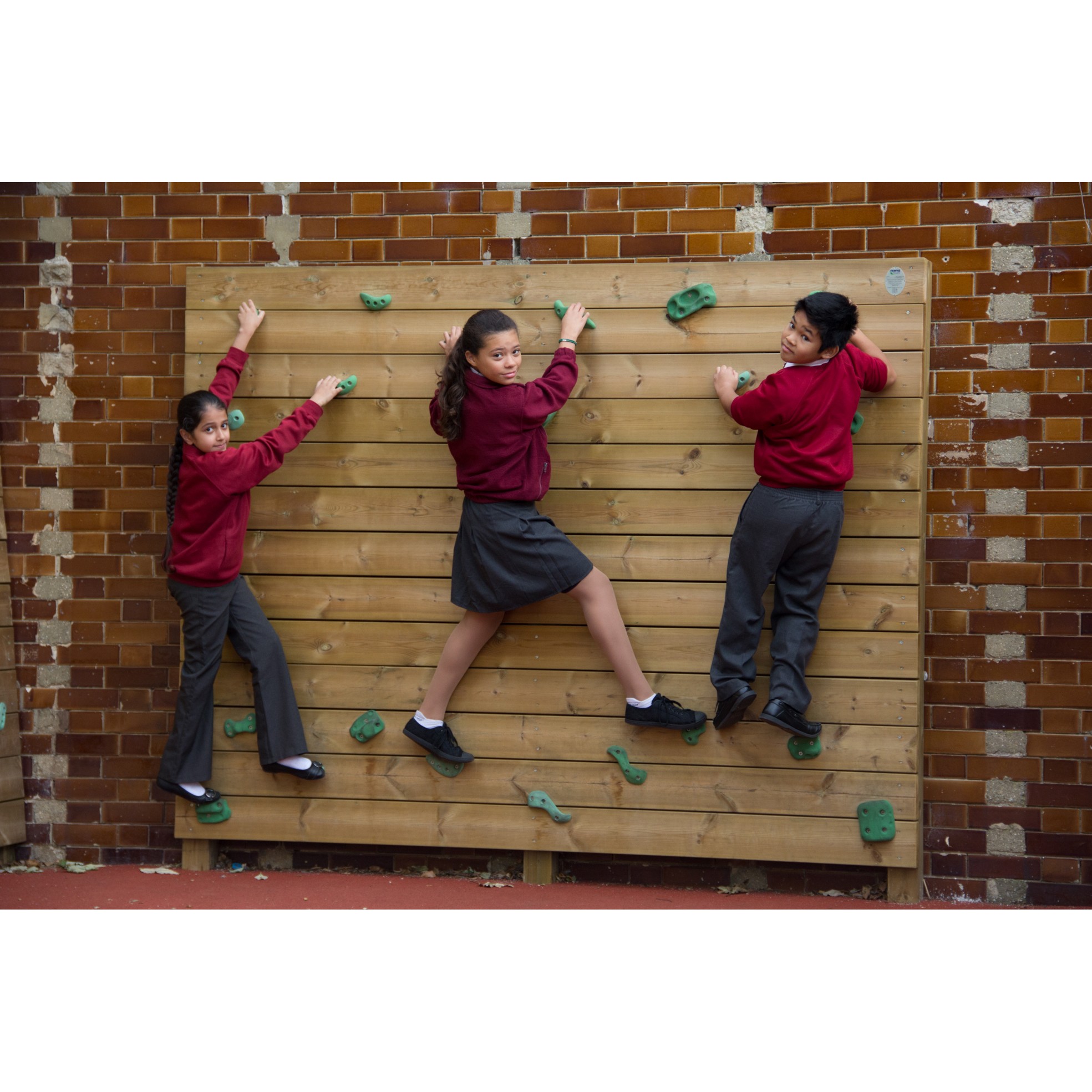 Three children in school uniforms climb a wooden Single Sided Bouldering Wall attached to a brick wall.