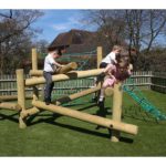 Three children in school uniforms climb and play on a wooden and rope climbing frame in an outdoor playground with artificial grass.