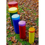 Five colourful outdoor drums of varying heights stand on grass surrounded by autumn leaves.