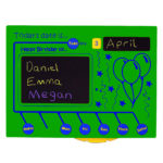 A green board displays the date as Tuesday, 3 April. It lists birthdays for Daniel, Emma, and Megan, and includes balloon drawings. Days of the week are shown at the bottom.