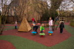 Several children play on colourful, Durabond mushroom-shaped stools and climbing structures in an outdoor playground with artificial grass and trees.