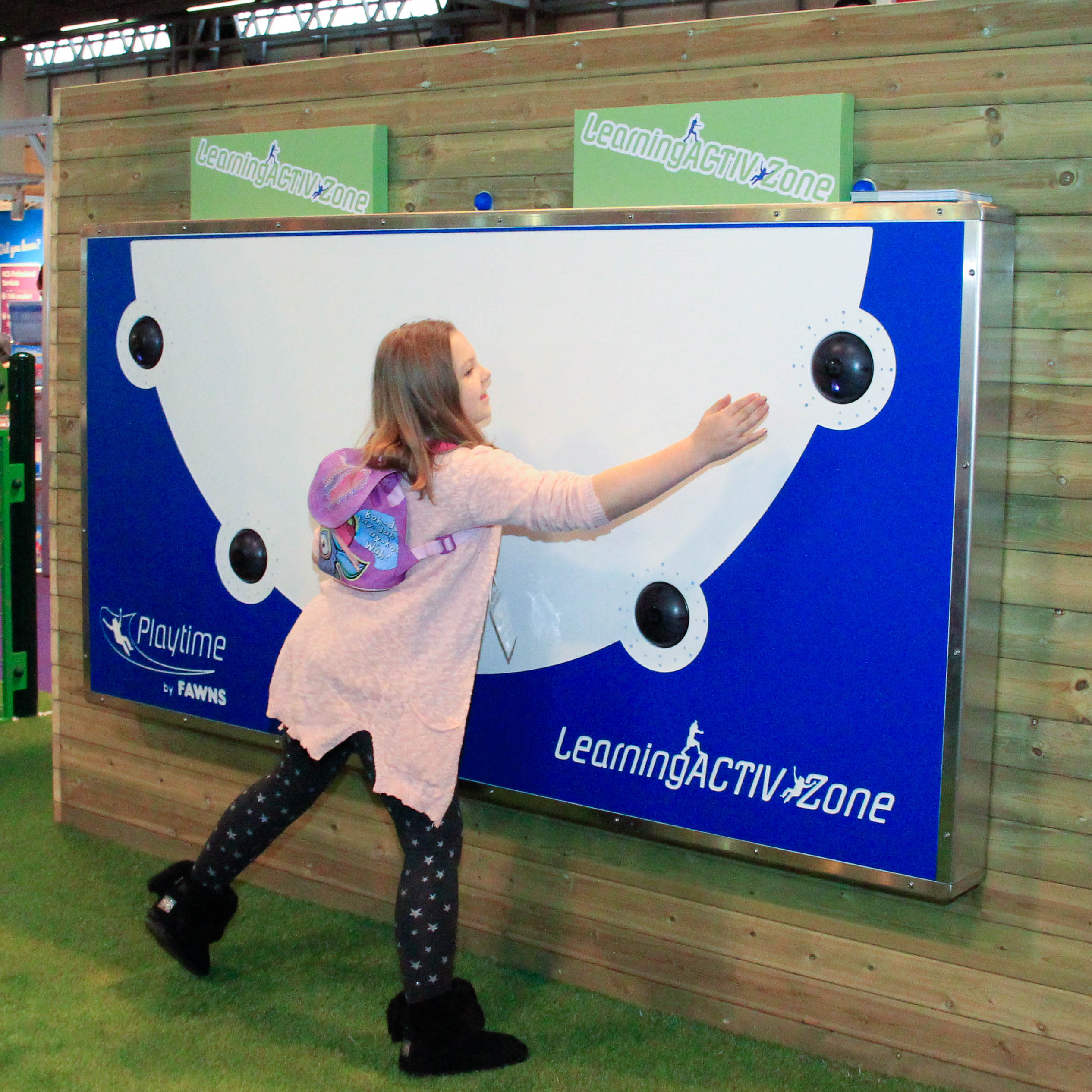A girl touches a blue and white interactive wall panel labelled Learning ACTIVzone in an indoor play area.