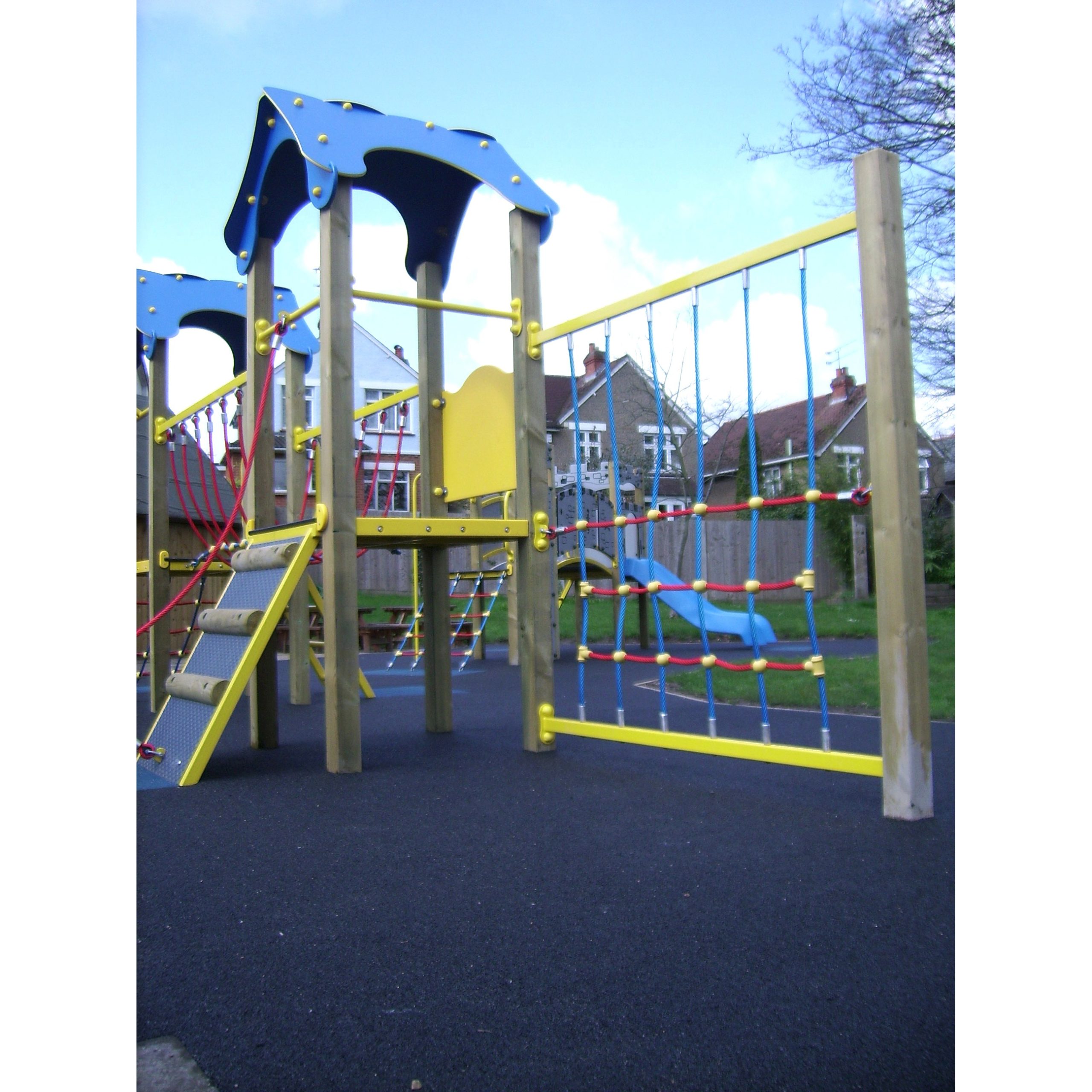 The Meteor Tower 900mm outdoor playground structure features climbing nets, a ladder, and a slide, all set on a black rubber surface with houses and trees in the background.