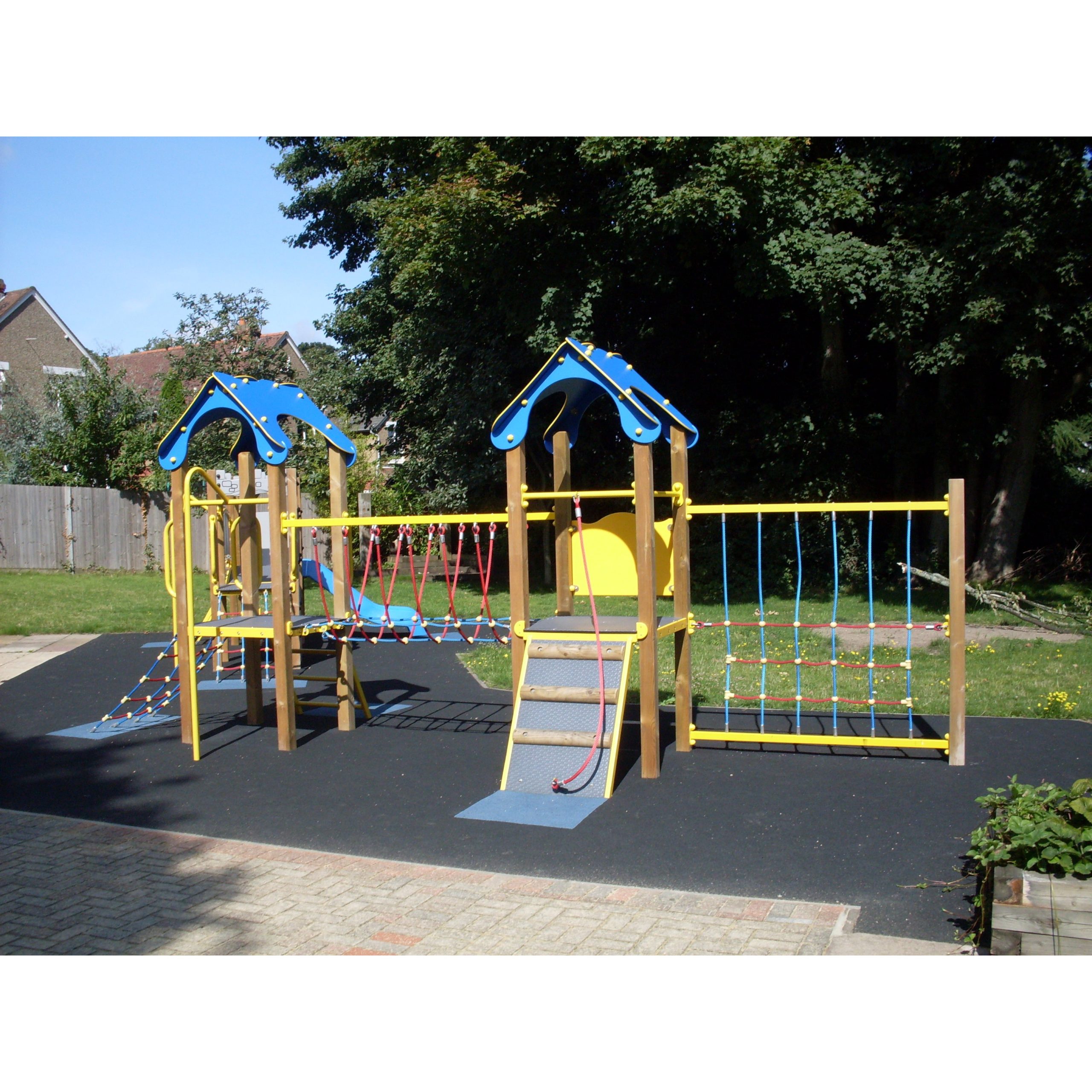 Outdoor playground set featuring blue and yellow climbing structures, including the Meteor Tower 900mm, with rope bridges and slides on a rubber safety surface near trees and a grassy area.