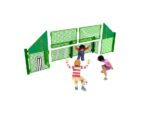 Three children play football near a green metal fence with target circles and a goal painted on it.