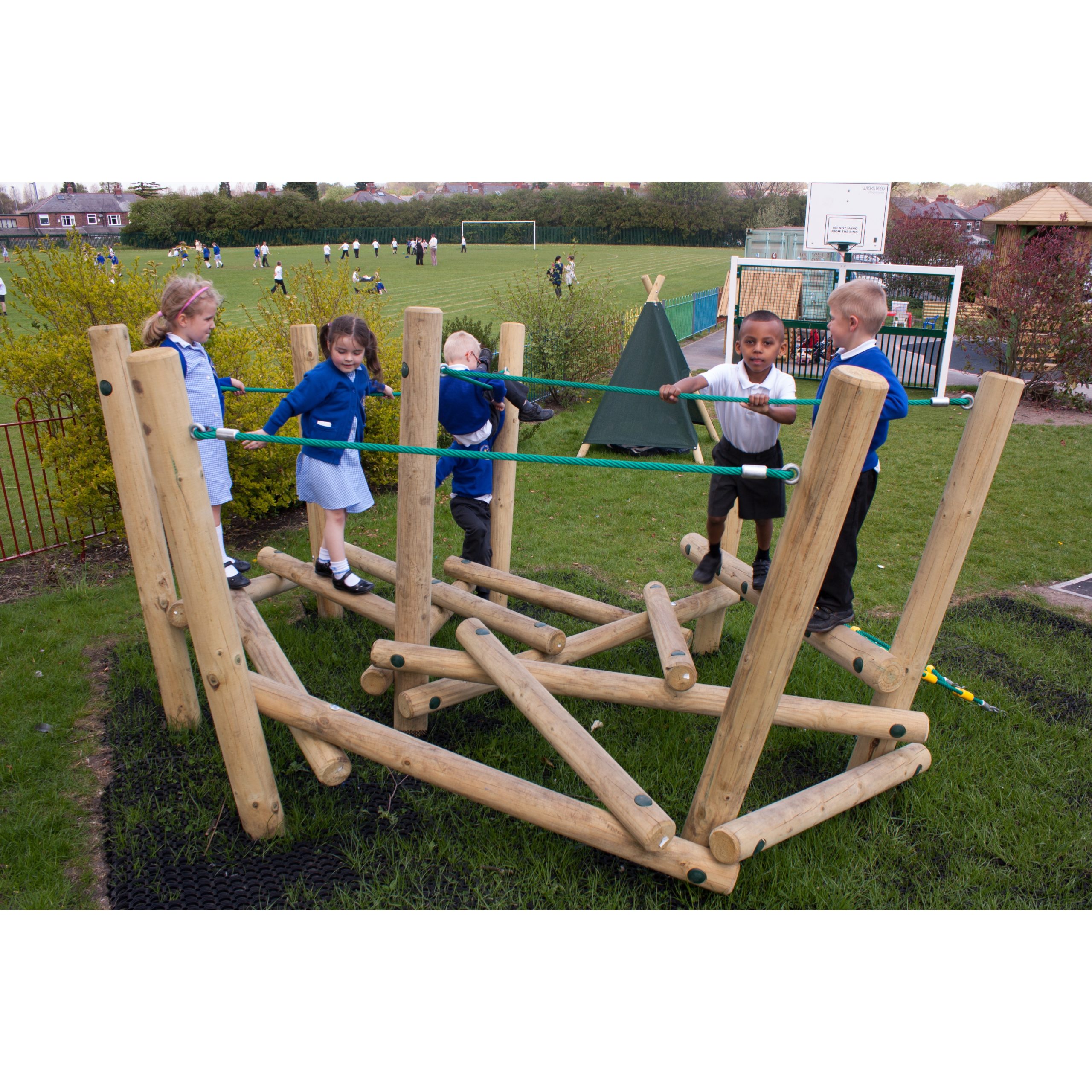 Five young children in school uniforms play on a wooden climbing frame outdoors, with a grassy field and other children in the background, reminiscent of the classic fun found with Pick Up Sticks 1.