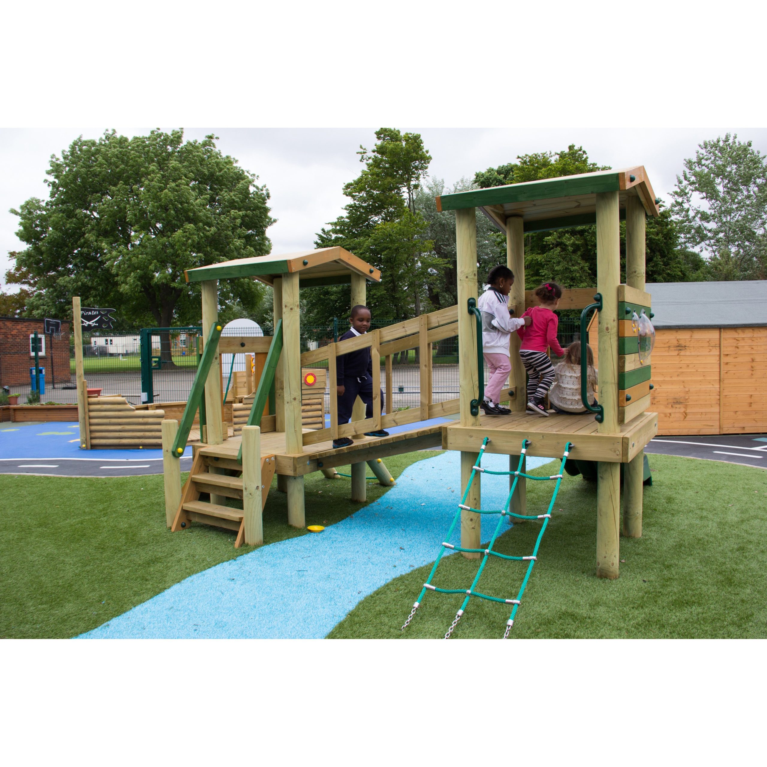 Several children play on a wooden playground structure with ladders, ramps, and a bridge on an artificial grass and rubber surface outdoors.