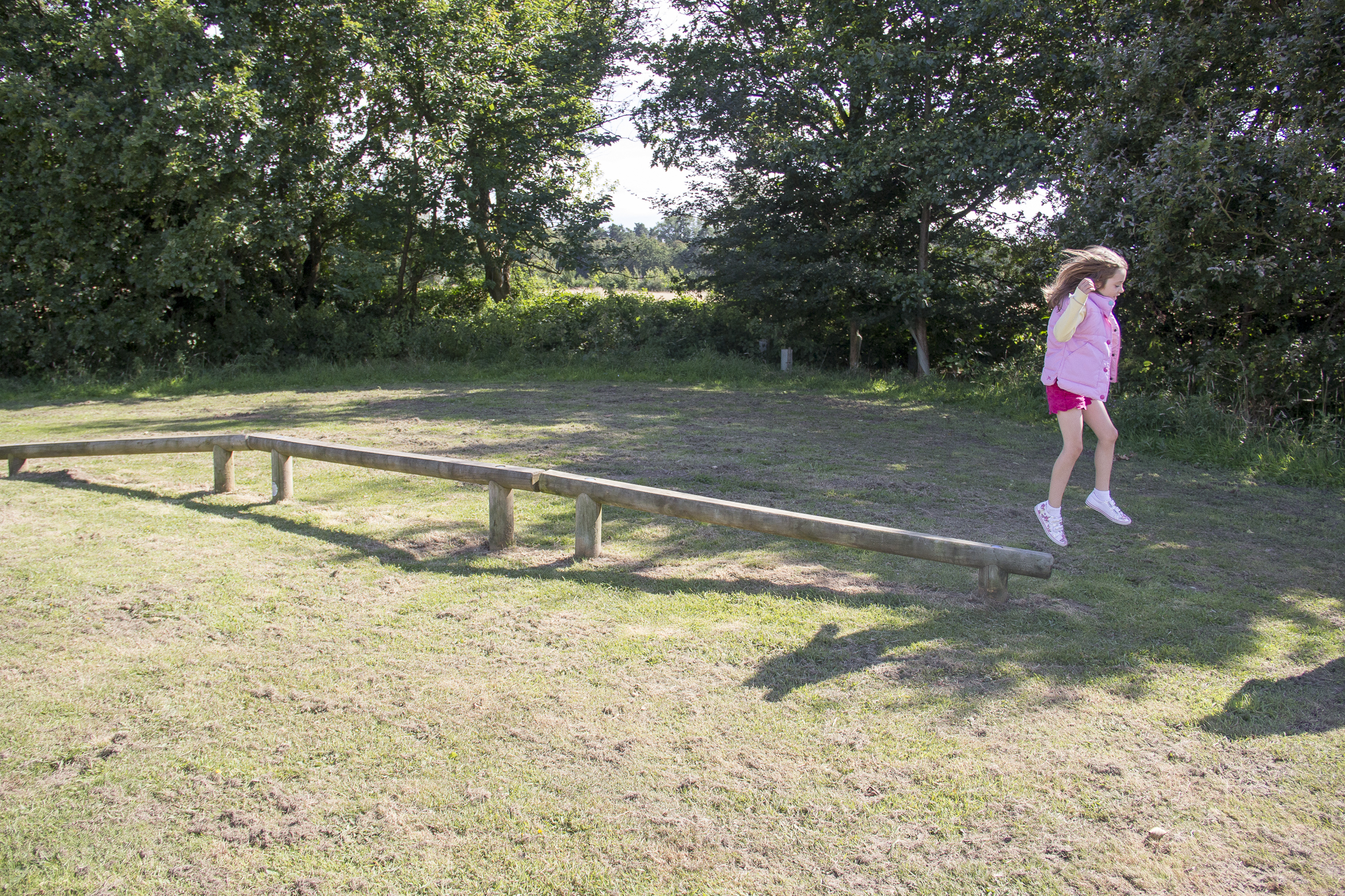 child in a pink top and red shorts jumping off the end of the balance run