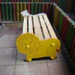 A wooden bench with a lion shape on one end and a white animal shape on the other, surrounded by colourful vertical wooden posts.