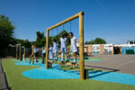 Children in school uniforms play on a wooden climbing frame in a school playground with artificial grass, blue markings, and clear skies—capturing the spirit of adventure found on the Essential Madagascar Trail.