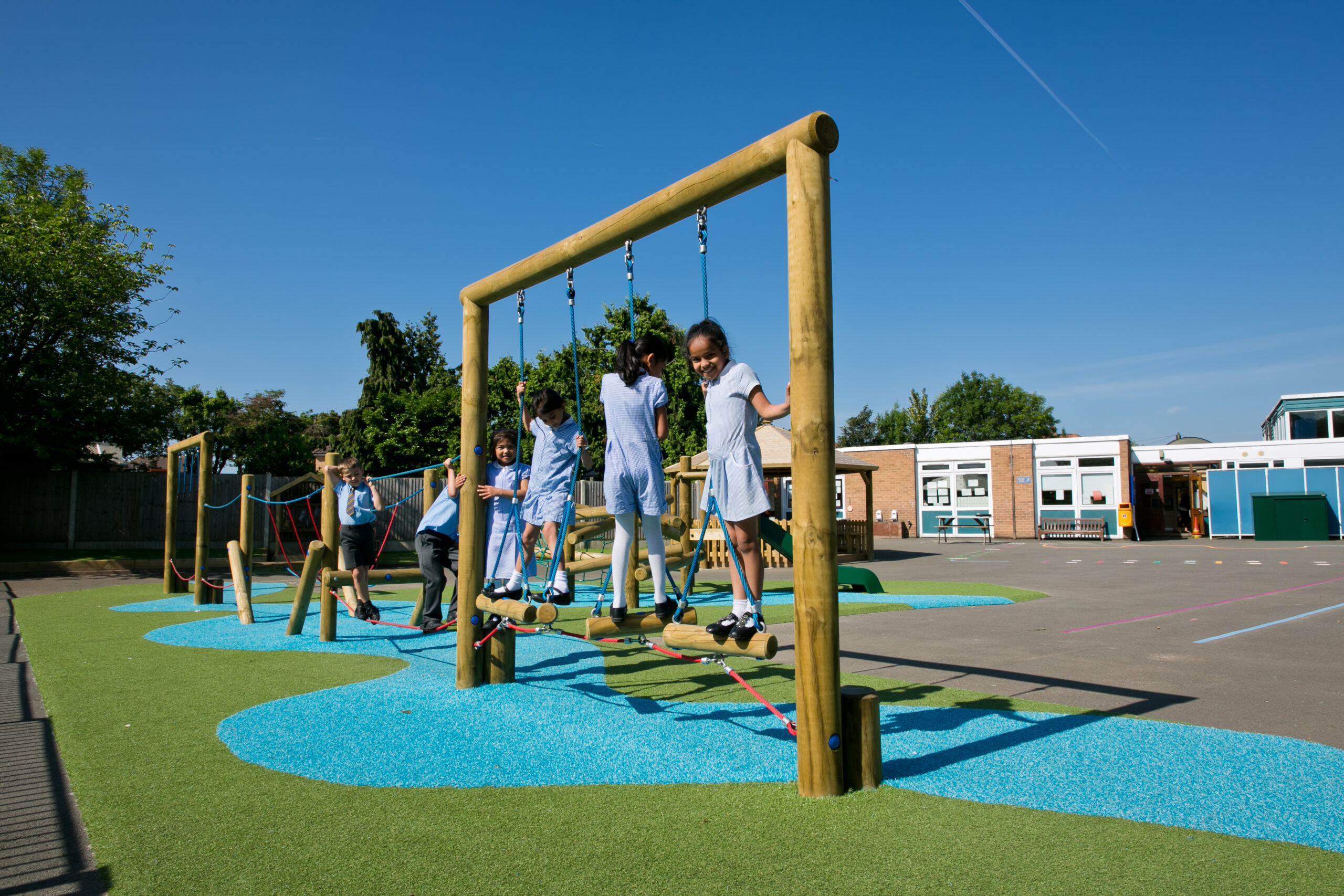 Children in school uniforms play on a wooden climbing frame in a school playground with artificial grass, blue markings, and clear skies—capturing the spirit of adventure found on the Essential Madagascar Trail.