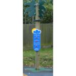 A wooden post shaped like a palm tree with a weather information board attached, standing on grass near a wooden fence.