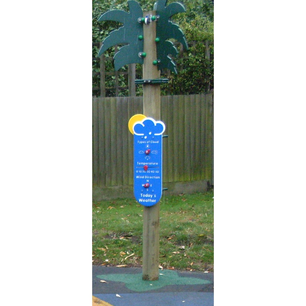A wooden post shaped like a palm tree with a weather information board attached, standing on grass near a wooden fence.