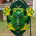 A frog-shaped outdoor thermometer with green and yellow colours is mounted on a vertical wooden post.