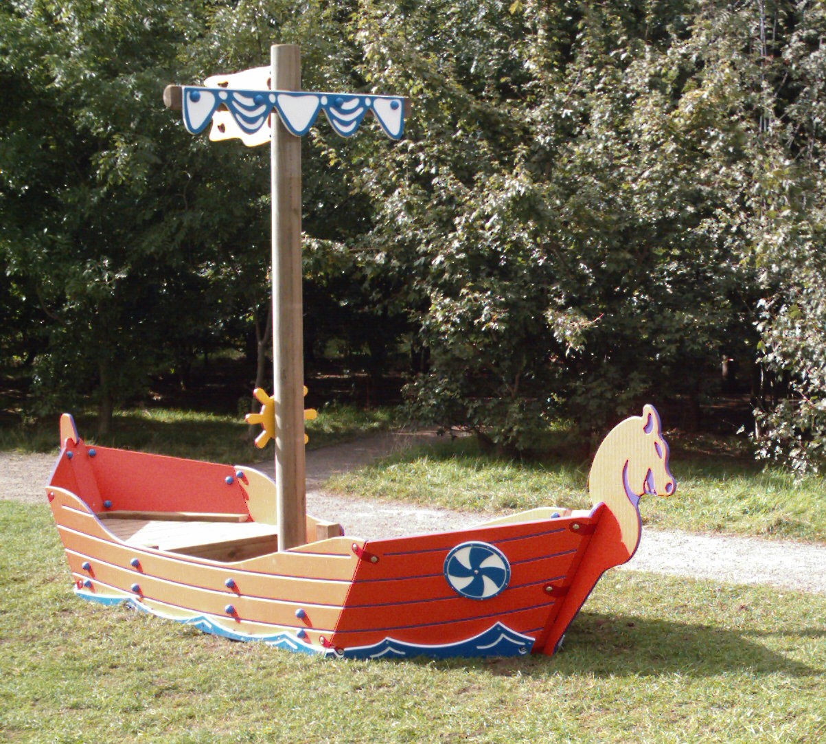 Wooden playground structure shaped like a Viking ship with painted details, set on grass near a path and trees in the background.