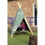 Two children sit inside a small, triangular outdoor play structure resembling a tipi on artificial grass near a brick building.
