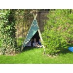 Three children sit inside a small, green tepee tent in a sunny garden with artificial grass, bushes, and a brick wall in the background.