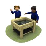 Two children stand by a wooden water table with a glass top, set on a patch of grass. One child waves whilst the other reaches towards the table, eager to explore and play.