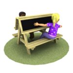 Two children sit at a wooden picnic table with a chalkboard divider on a circular patch of grass, facing opposite sides.