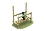 A child crosses a wooden Link Clatter Bridge playground structure, holding onto a horizontal support bar for balance, on a patch of artificial grass.