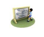 A young child stands on grass interacting with a vertical wooden marble run board featuring angled tracks.