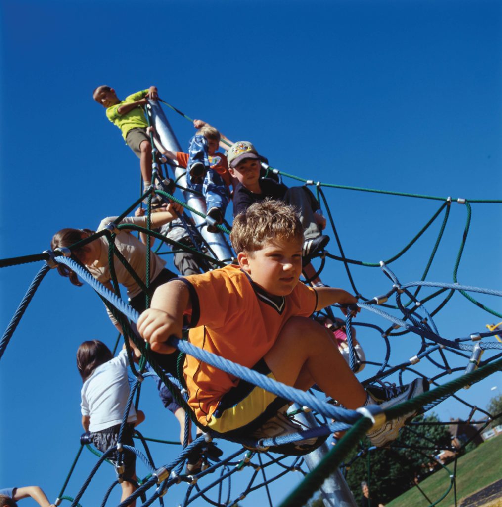 Children climbing on a rope play structure outdoors under a clear blue sky.