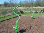 Two spiral playground spinners on mulch ground, surrounded by a fence and trees in the background under a clear sky.