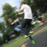 Two people spinning on a playground equipment with blurred motion, smiling and having fun at a park.