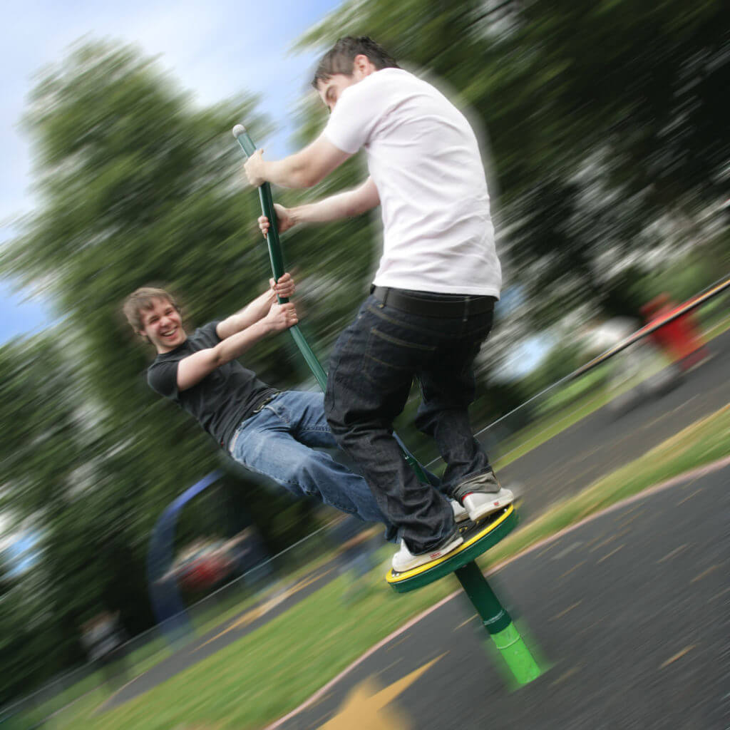 Two people spinning on a playground equipment with blurred motion, smiling and having fun at a park.