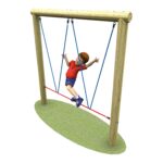 Child wearing a red shirt and blue shorts swings on a wooden log swing set with blue ropes, over an oval patch of grass.