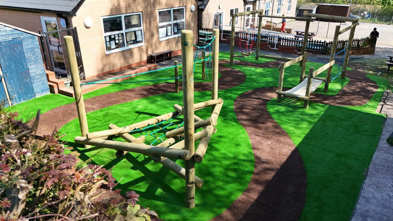 Outdoor playground with climbing structures, rope bridges, and green artificial turf next to a building under daylight.