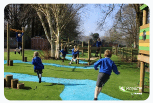 Children in blue uniforms play on outdoor playground equipment under trees, with a blue rubber path and grass, during a sunny day.