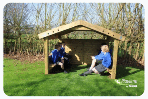 Four children in blue school uniforms sit and talk inside a small wooden shelter on grass, with leafless trees in the background. Playtime by FAWNS logo is visible in the lower right corner.