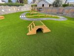 A playground with artificial grass, wooden climbing structures, and a winding bike or scooter path painted to look like a road.