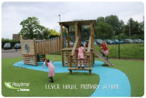 Three children in pink uniforms play on a wooden climbing structure with blue safety surfacing, showcasing creative playground ideas for primary schools at Lever House Primary School’s outdoor playground.