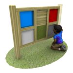 A child kneels on grass in front of a Tactile Sensory Board – 6 Panels, featuring wooden sections with different colours and textures.