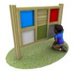 A child kneels on grass, interacting with a sensory panel that has coloured and textured squares framed in wood.