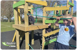 Three children play on a wooden climbing frame outdoors. One boy smiles at the camera, holding onto green ropes. The Playtime by FAWNS logo appears in the bottom left corner.